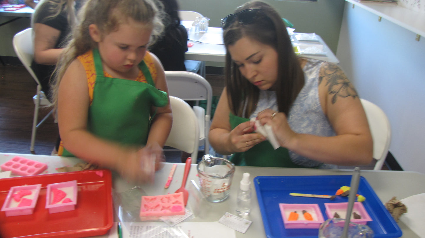 A woman and a child working with soap dough and meltable soap to create bar soaps.